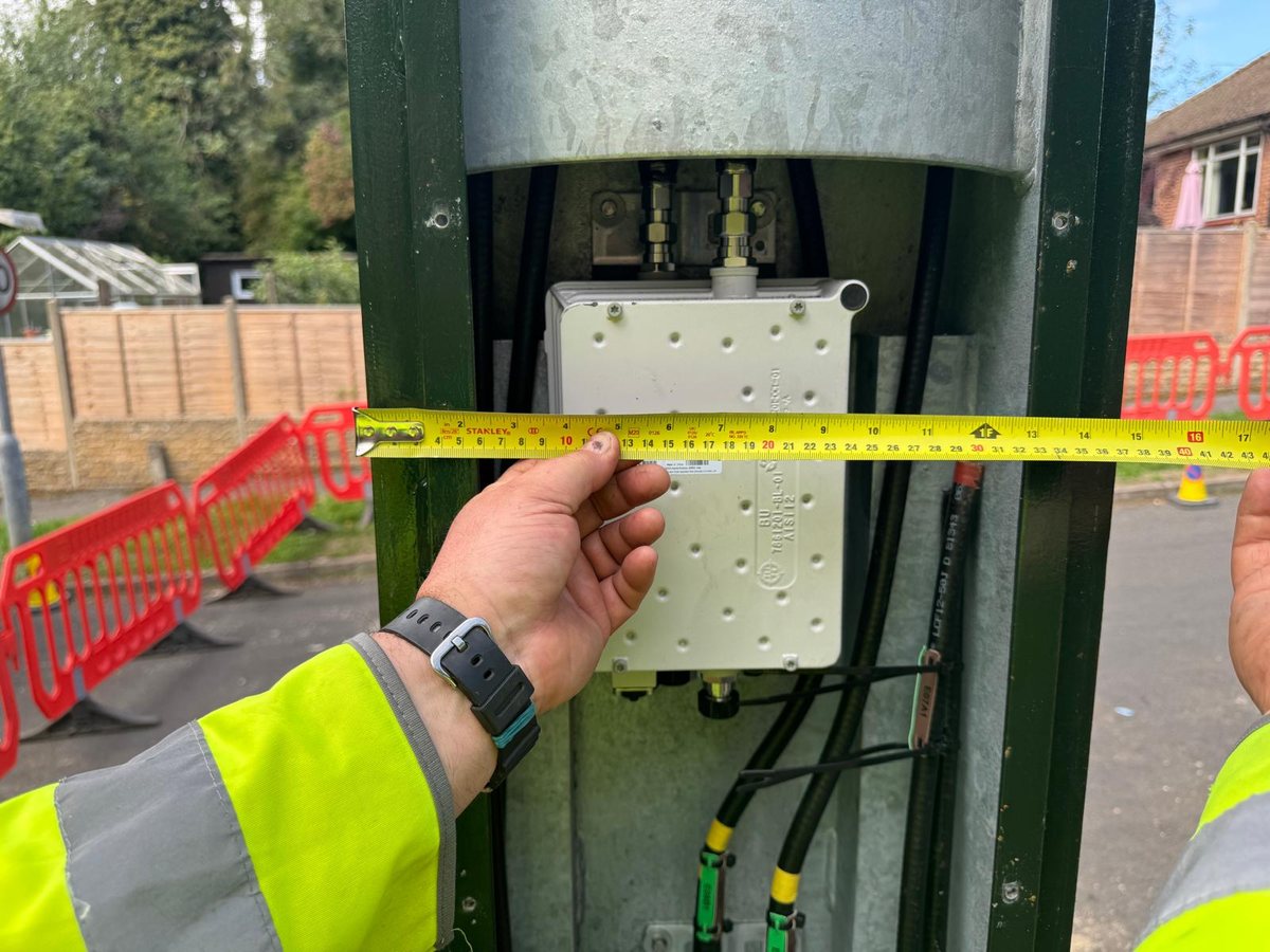 A steel tape held across the open equipment door of the new mast's base enclosure, showing radio equipment inside, reading about 36 to 37 centimetres between the edges of the frame